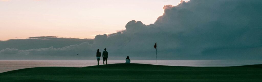 海に面したグリーン、夕日を見る、立つ２人の人間と座っている１人の人間の画像