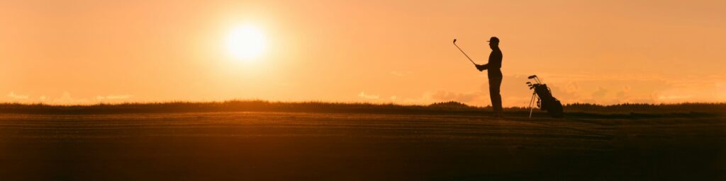 １人のゴルファーが夕日を背景に立っている画像